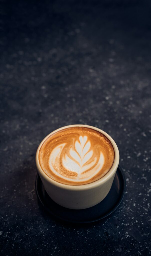 Close up hot capucino coffee cup with latte art foam on black stone table at cafe